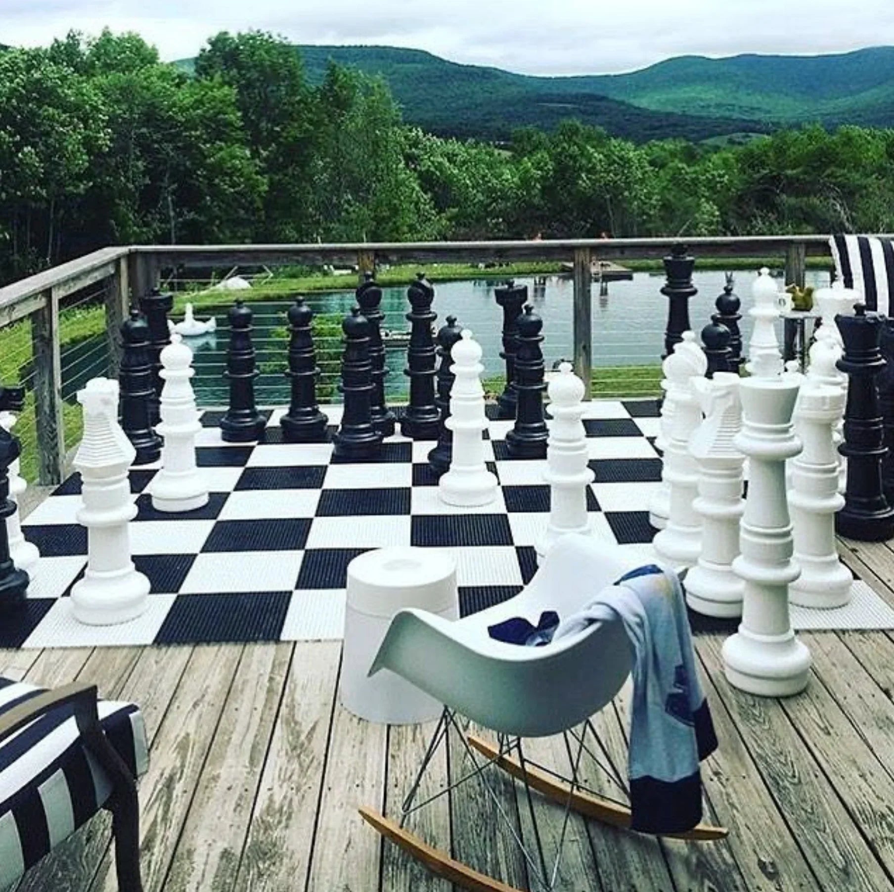 giant outdoor chess set on deck overlooking lake and mountains beside modern rocking chair