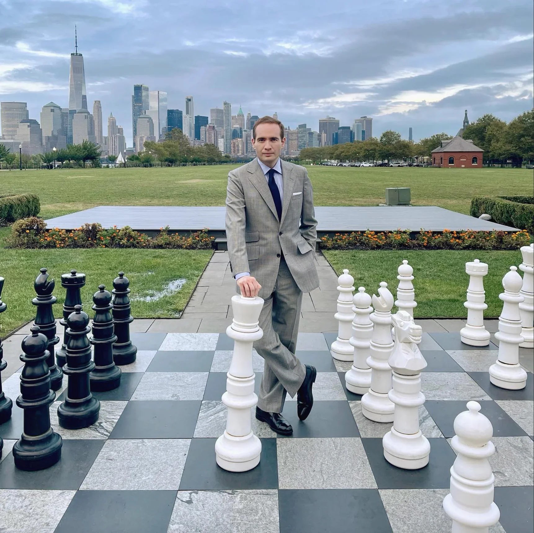 photo man in suit standing on giant outdoor chessboard with city skyline behind black and white pieces illustrating does chess help with business