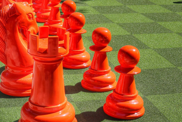 bright-orange-giant-chess-pieces-including-pawns-rook-and-knight-on-green-turf-showcasing-a-colorful-giant-chess-set-for-christmas-outdoors