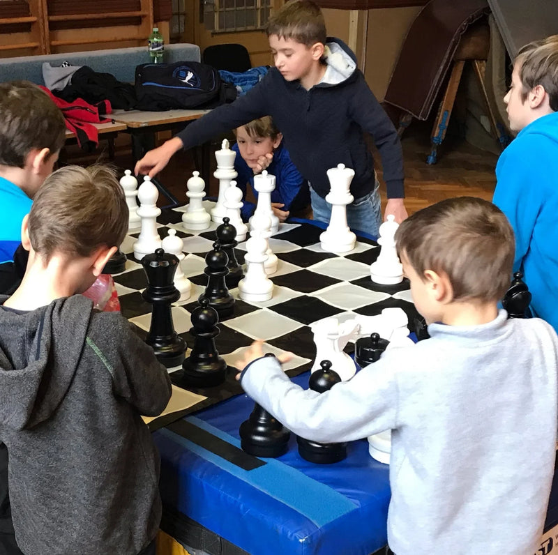 children-gather-around-a-giant-chess-set-indoors-while-moving-black-and-white-pieces-on-a-large-board