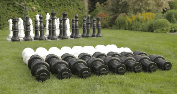 Giant black and white chess pieces arranged on green grass outdoor garden with trees and bushes in background showcasing how to make giant chess pieces taller and more visible.