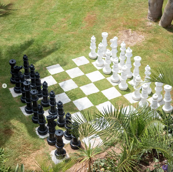 Giant chess set on grass board with white marble squares surrounded by palms showing how big is a chess board for lawn and garden play.