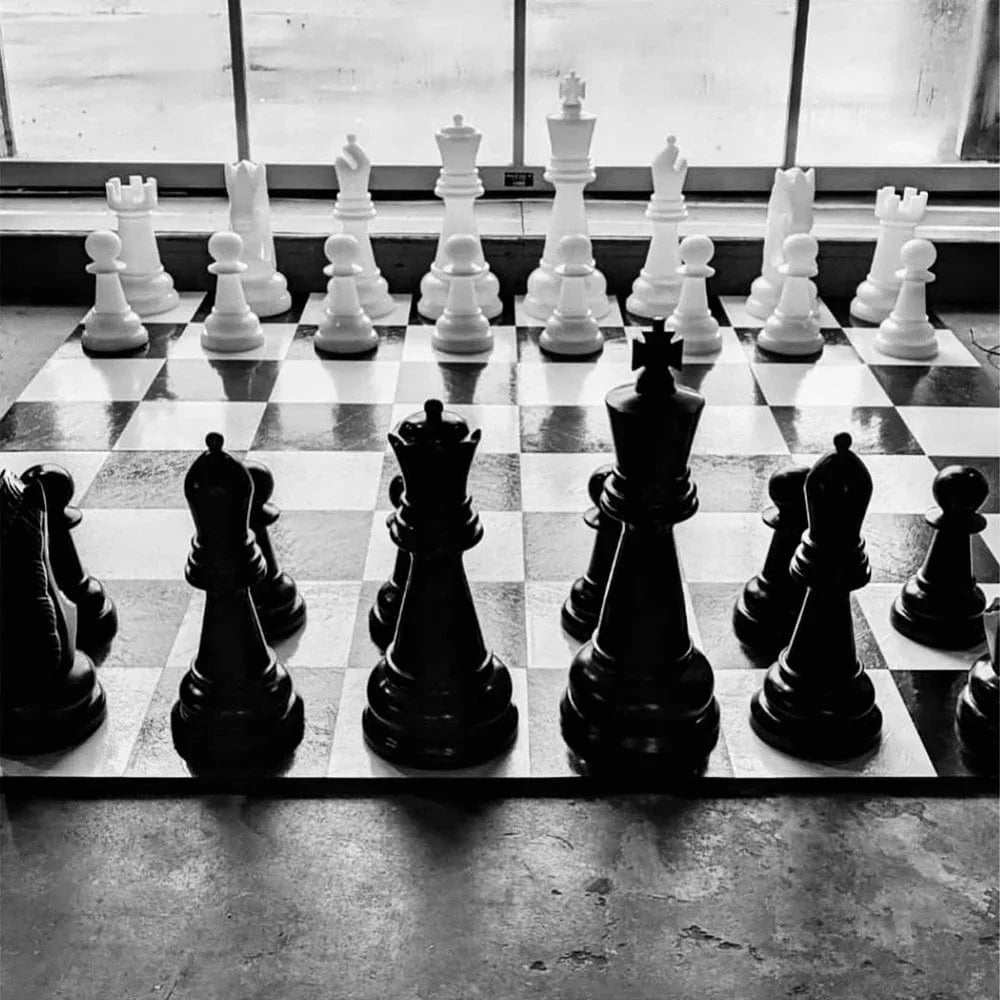 giant-chess-set-with-black-and-white-pieces-arranged-in-starting-position-demonstrating-how-to-set-up-a-chessboard-on-a-checkered-board-in-front-of-a-window