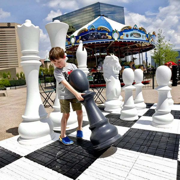 young-boy-lifting-a-large-black-pawn-on-an-outdoor-chessboard-demonstrating-how-big-are-chess-pieces-in-a-life-size-chess-set