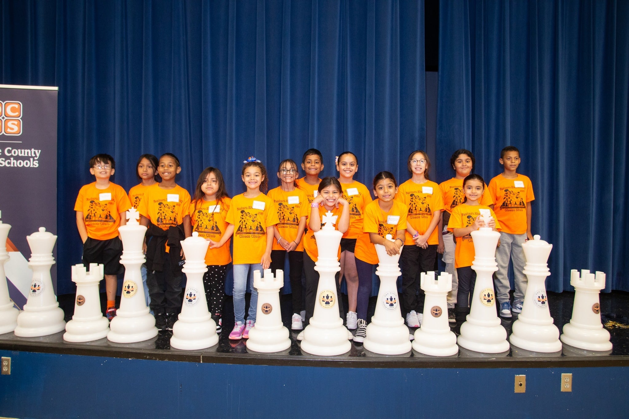 Group of students with oversized chess pieces, celebrating Chess Trophies at an event.
