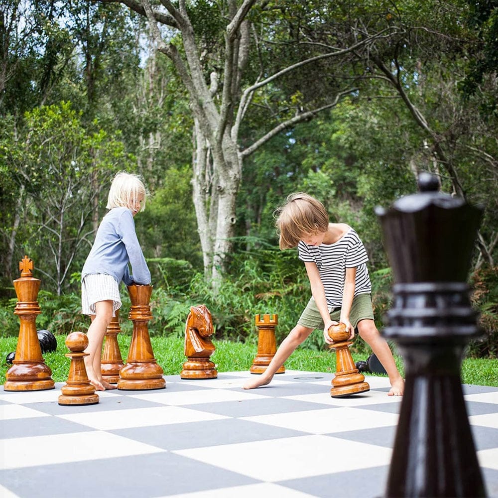 Children playing with Two Foot Tall Teak Giant Chess Sets in an outdoor setting.