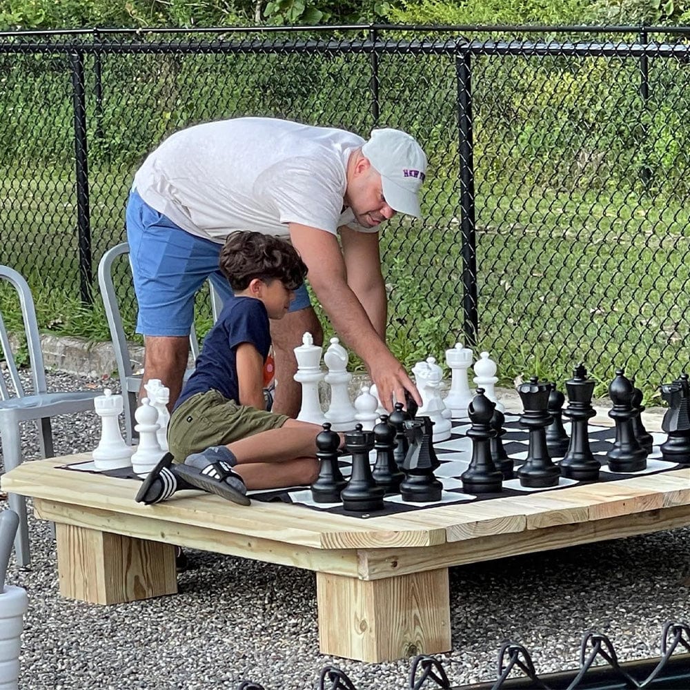 A man and a child playing on a large chess set outdoors, highlighting the enjoyment of 12 Inch Large Chess Sets.