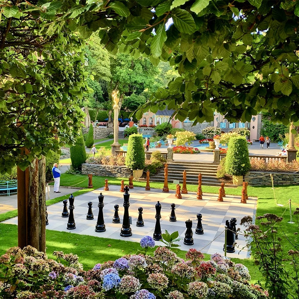 Six Foot Tall Teak Giant Chess Sets displayed in a beautiful garden setting, surrounded by flowers and lush trees.