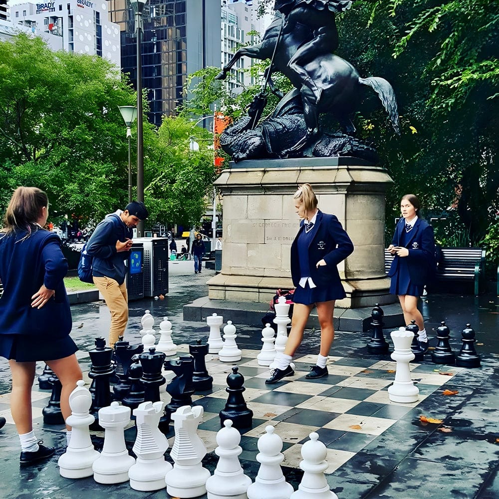 Group of people playing chess in a park with a statue in the background