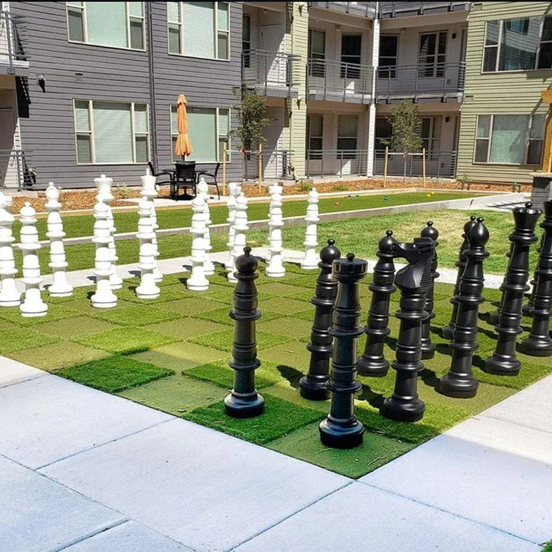 Large outdoor chess set with giant chess pieces on a grassy area in front of apartment buildings.