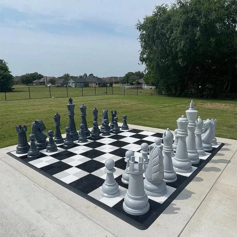 Large outdoor chess set with pieces on a checkered board in a park.