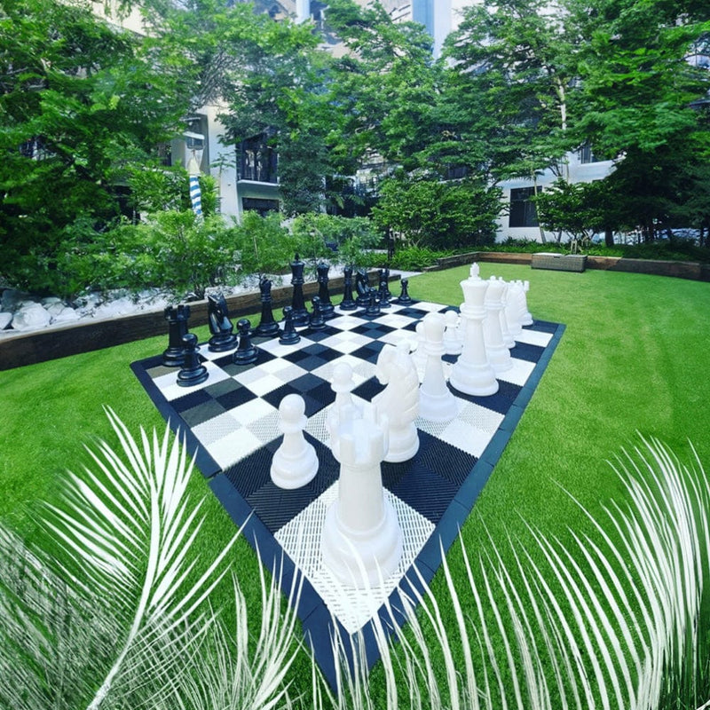 Large outdoor chess set with pieces on a grassy area surrounded by trees and buildings.