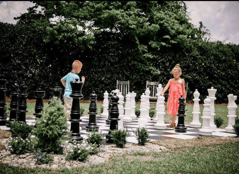 Two children playing with a large outdoor chess set in a park.